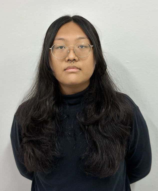 Profile picture of Emily: girl with long curly hair that flows in front of her, rocking a clip-on septum piercing, golden round spectacles, and a dark navy sweater. She looks somberly at the camera.