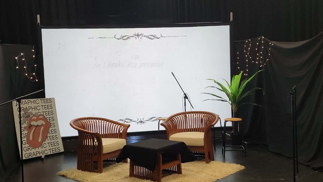 A set with two arm chairs in front of a projector screen and some light decors